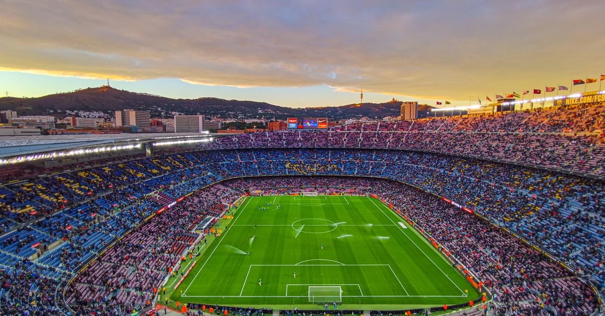 Aerial view of Camp Nou stadium filled with spectators during a football match at sunset in Barcelona, Spain.