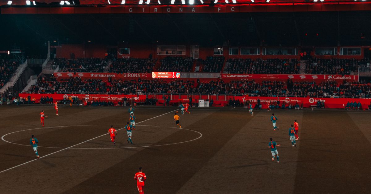 Wide-angle view of a soccer match taking place in a stadium at sunset with a vibrant sky.