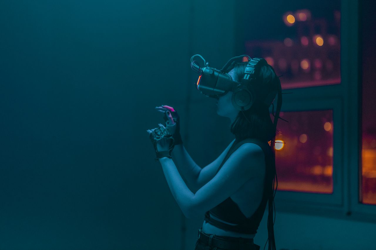 A woman wearing a VR headset and gloves immersed in a virtual reality experience inside a dimly lit room.